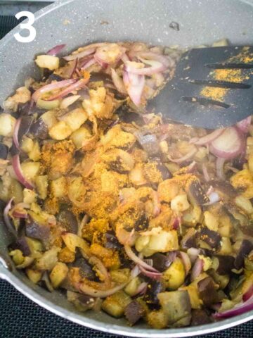 person stirring a pot of curry with aubergine in a large pan on the hob