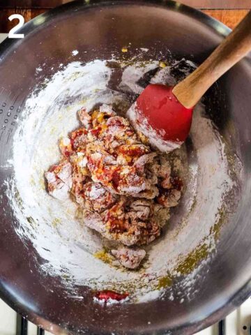 person coating beef strips with seasoned cornflour in a large mixing bowl with spatula