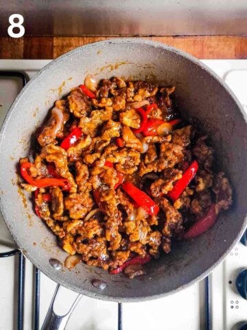 crispy beef strips coated in a homemade honey chilli sauce in a large pan on stove top before serving