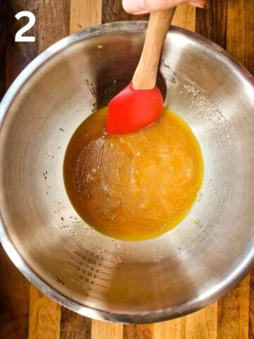 person mixing melted butter with granulated sugar in a large mixing bowl with red silicone spatula
