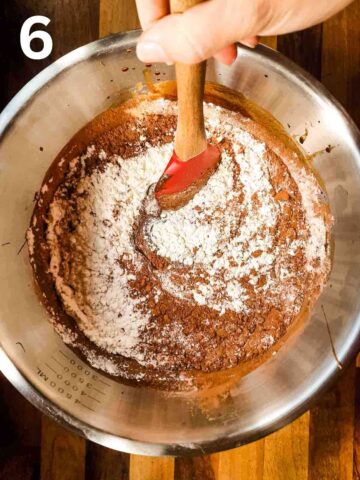 person stirring all purpose flour, cocoa powder and salt into a chocolate egg mixture