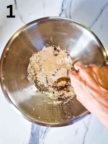 person mixing cornflour with Chinese 5 spice, salt and pepper in large stainless steel mixing bowl