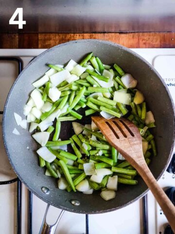 person stir frying green beans and chopped onions in a saute pan with wooden spoon