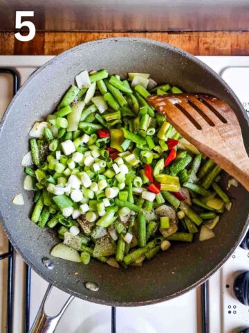 person frying vegetables with chillies, spring onions and salt and pepper in large frying pan