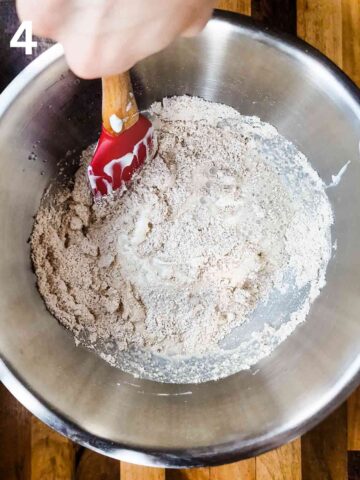 person mixing oatmeal scone dough together in a large stainless steel mixing bowl