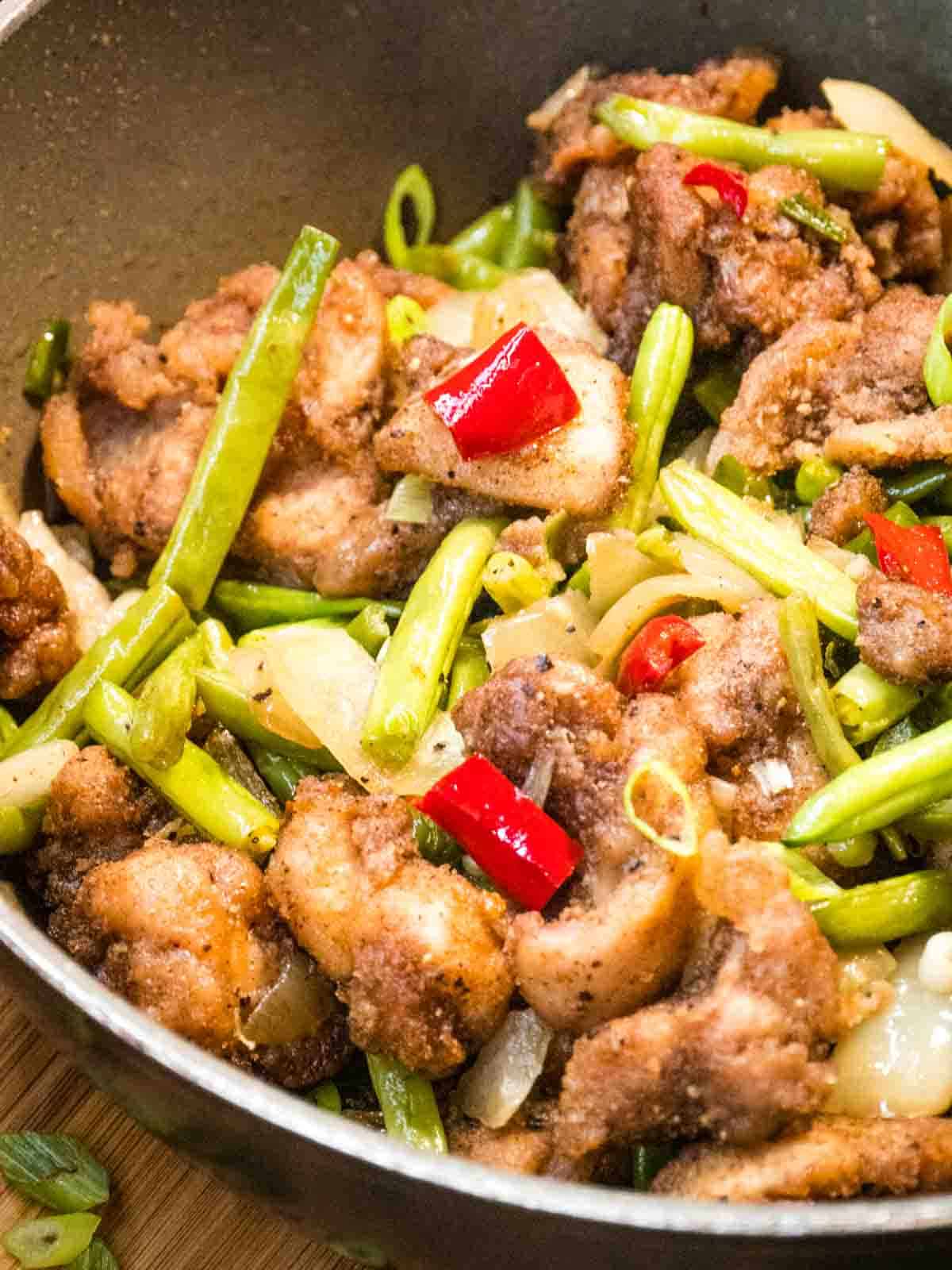 close up of Chinese salt and pepper chicken in a large grey skillet pan topped with spring onions and red chili peppers