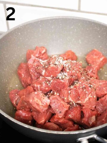 diced beef being seared in a frying pan with salt and pepper