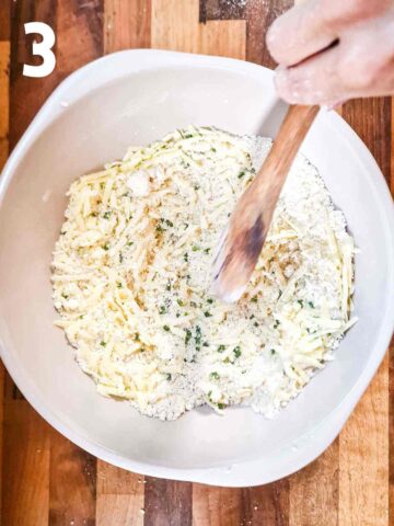 person stirring grated mature cheddar cheese and chives into a dry scone mix