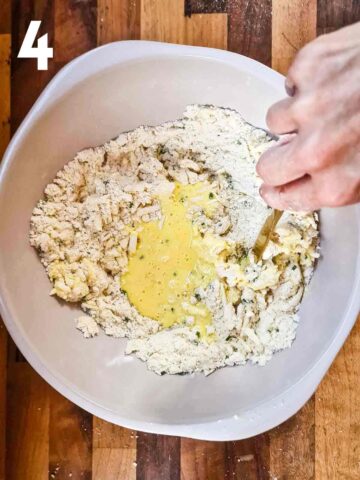 perspn stirring egg and buttermilk into a cheese scone mix using a knife to combine the wet and dry ingredients together
