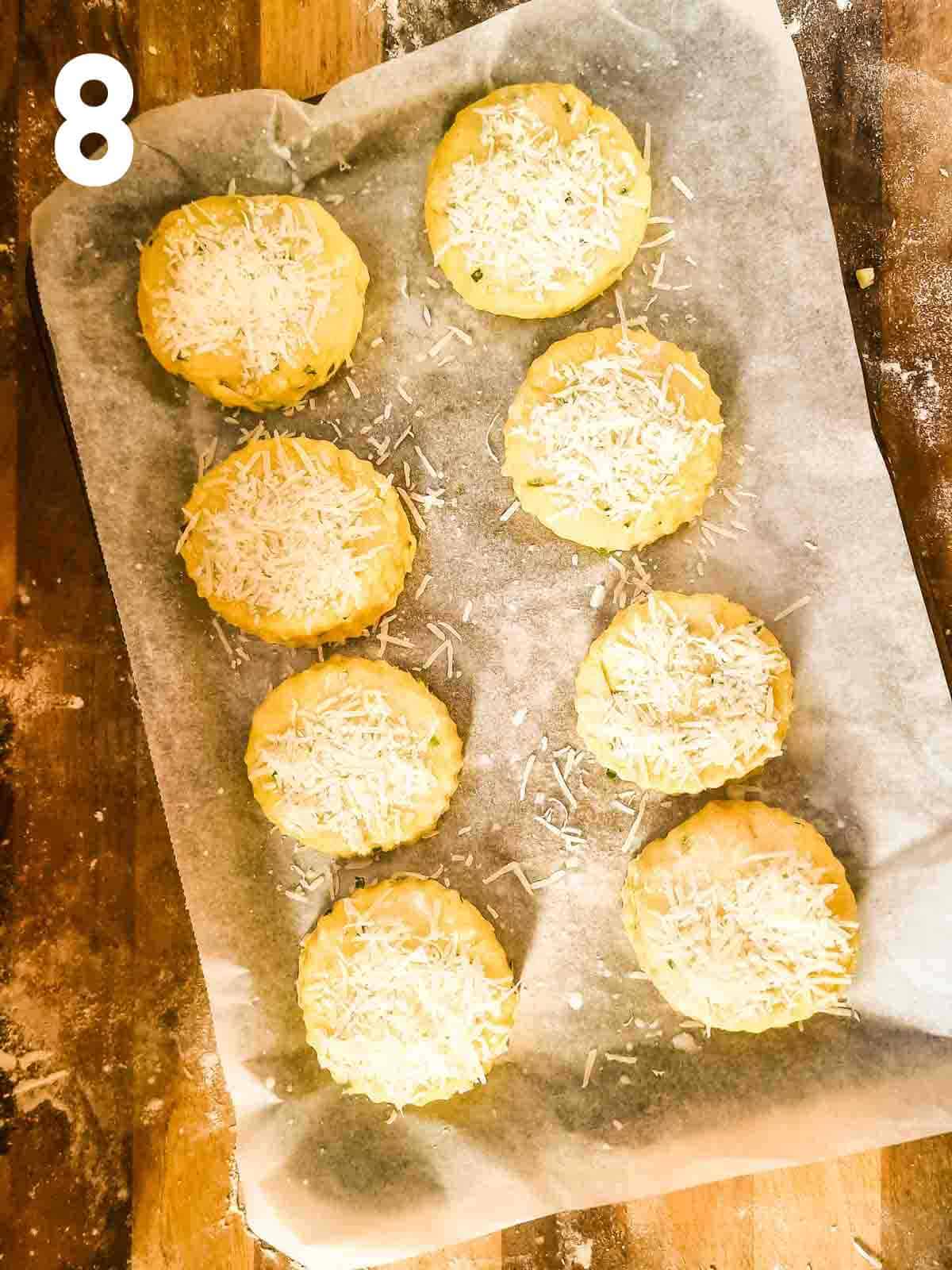 grated parmesan cheese on top of scones on a lined baking tray before baking in oven