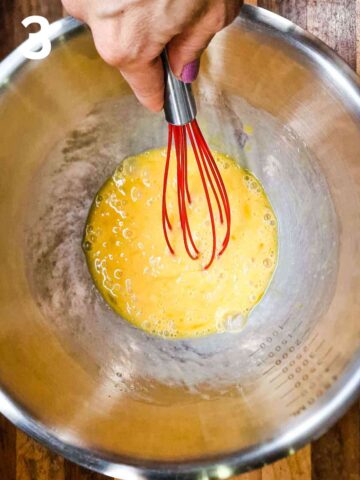 person whisking eggs in large stainless steel mixing bowl