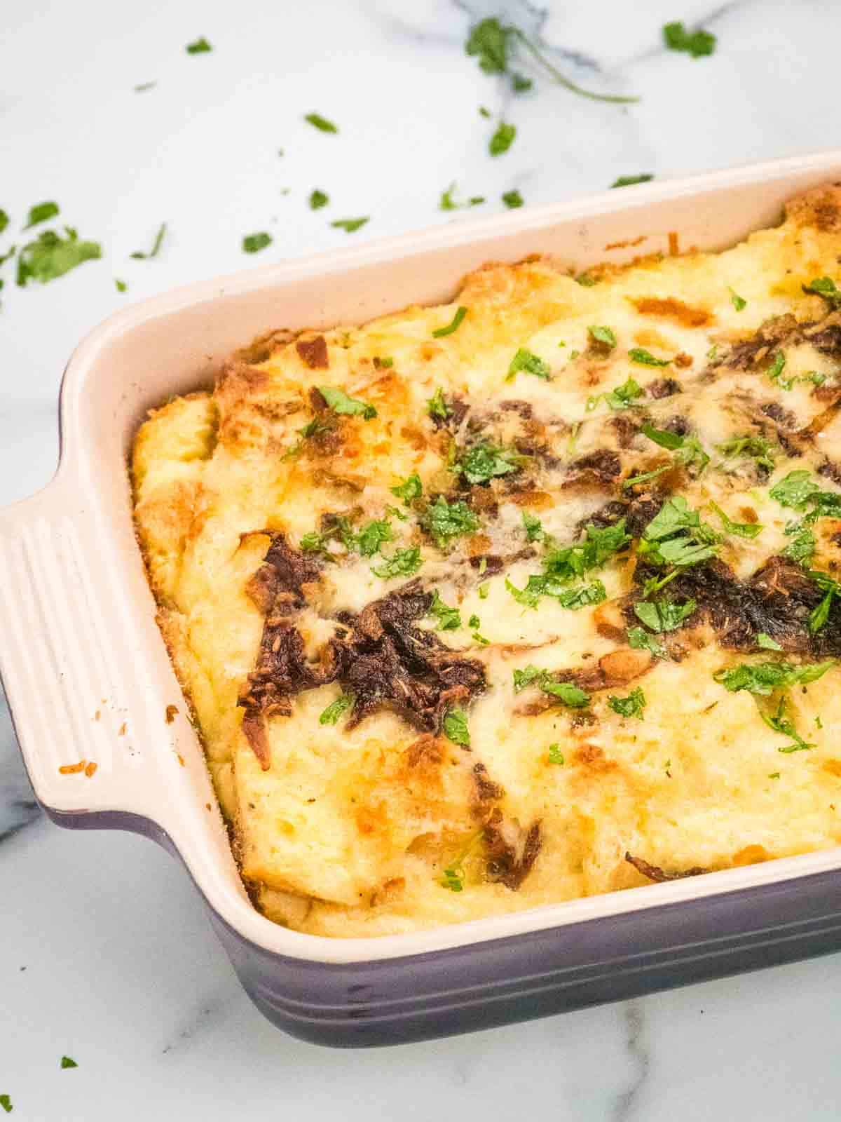 close up of baked bread with cheese, parsley, balsamic onions in purple Le Creuset dish