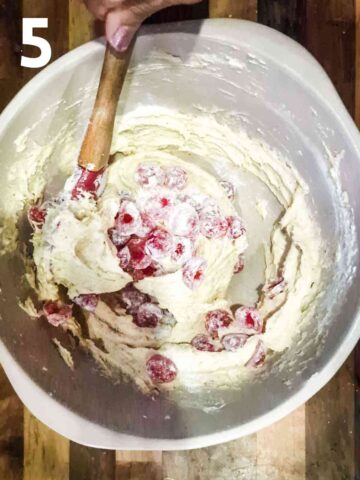 person gently stirring in halved gaced cherries into cake batter