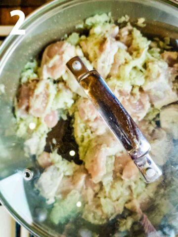person cooking diced chicken breast in onion paste in a covered frying pan