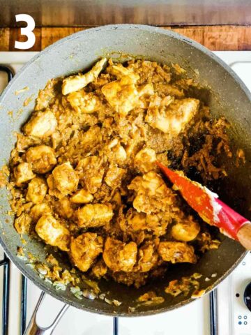 person cooking Indian spices in cooked chicken in frying pan