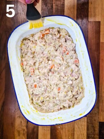 cool chicken pie filling in a pie dish while also brushing beaten egg on pie rim