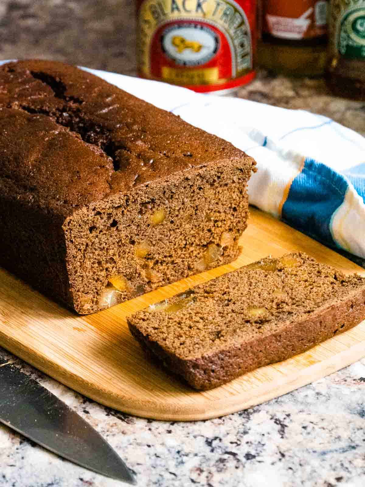 close up of stem ginger chunks visible in a ginegr loaf cake surrounded by a tin of black treacle, golden syrup, stem ginger and a blue, white and yellow tea towel on kitchen worktop