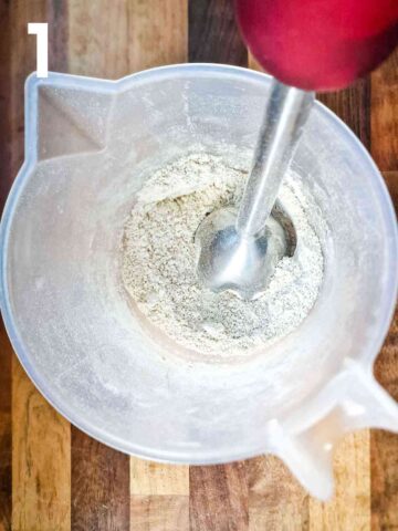 person milling porridge oats into oat flour with a stick blender in a large jug