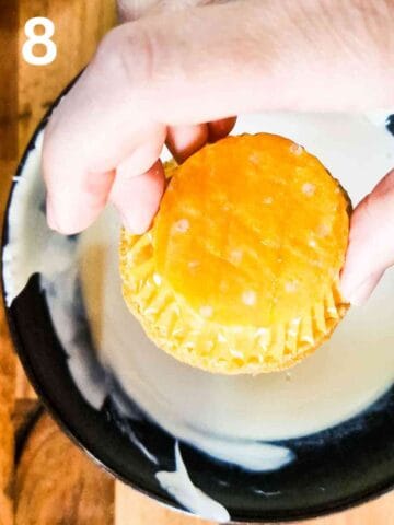 person dipping the tops of lemon cupcakes in lemon icing sugar to decorate