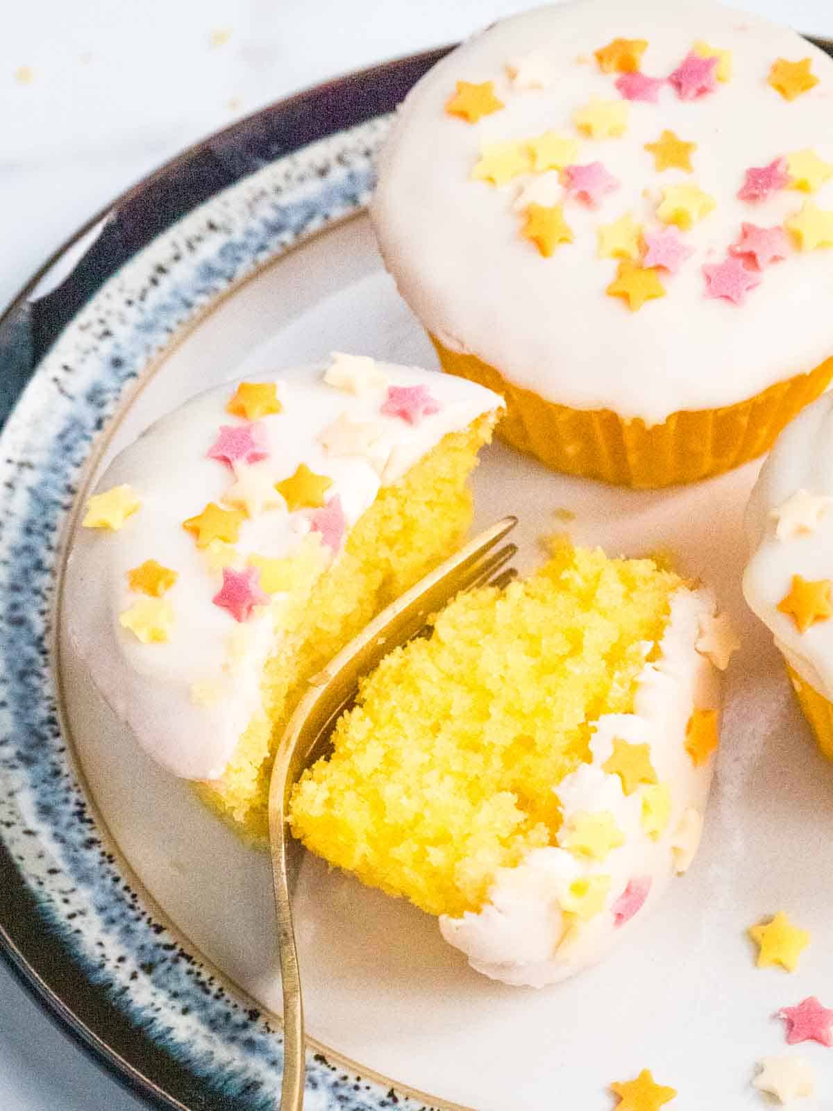person breaking a lemon drizzle cupcake with a fork after removing the cupcake paper