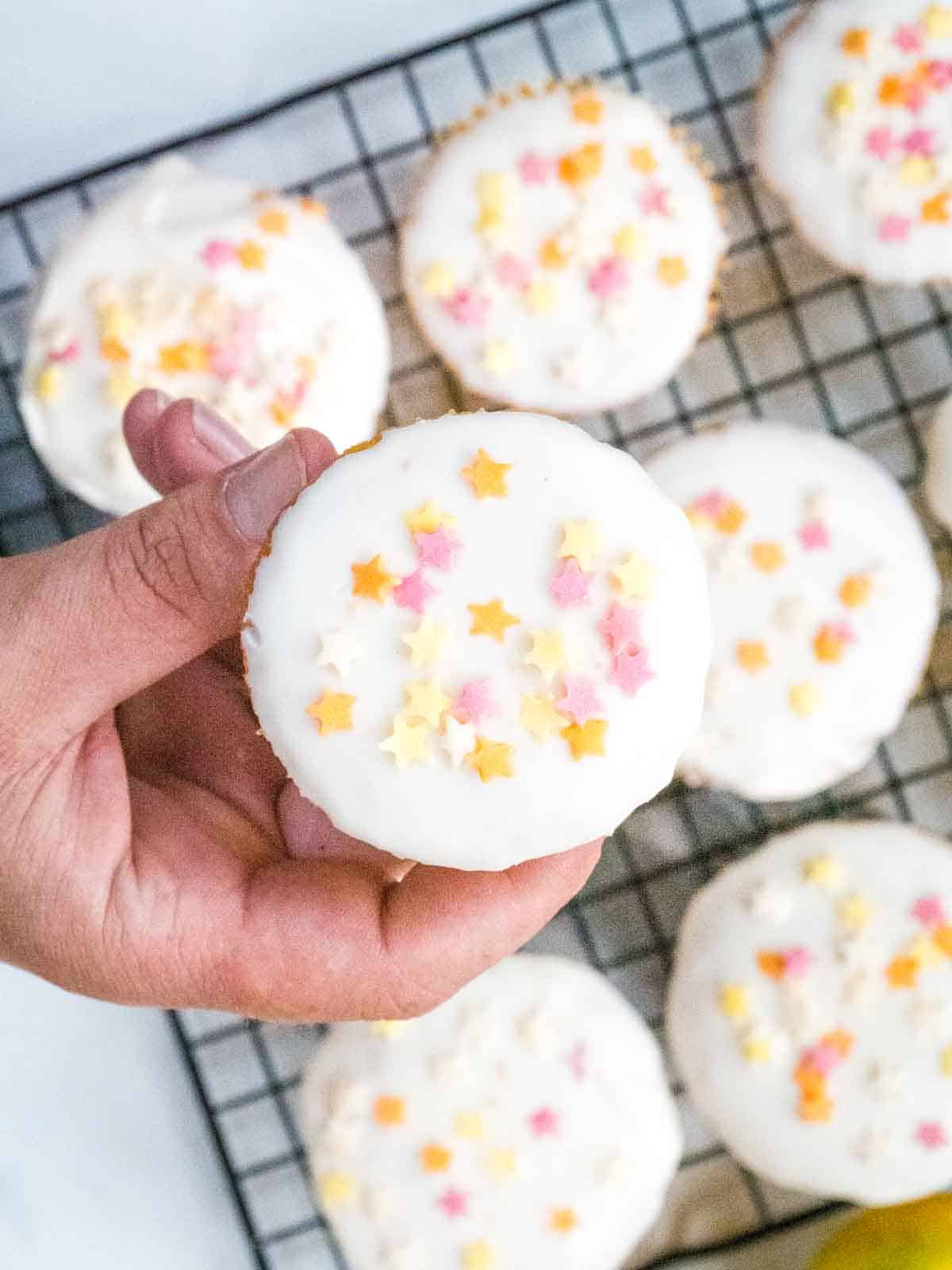 person holding an easy decorated lemon drizzle cupcake with vanilla and lemon icing sugar and candy multicoloured star shape sprinkles
