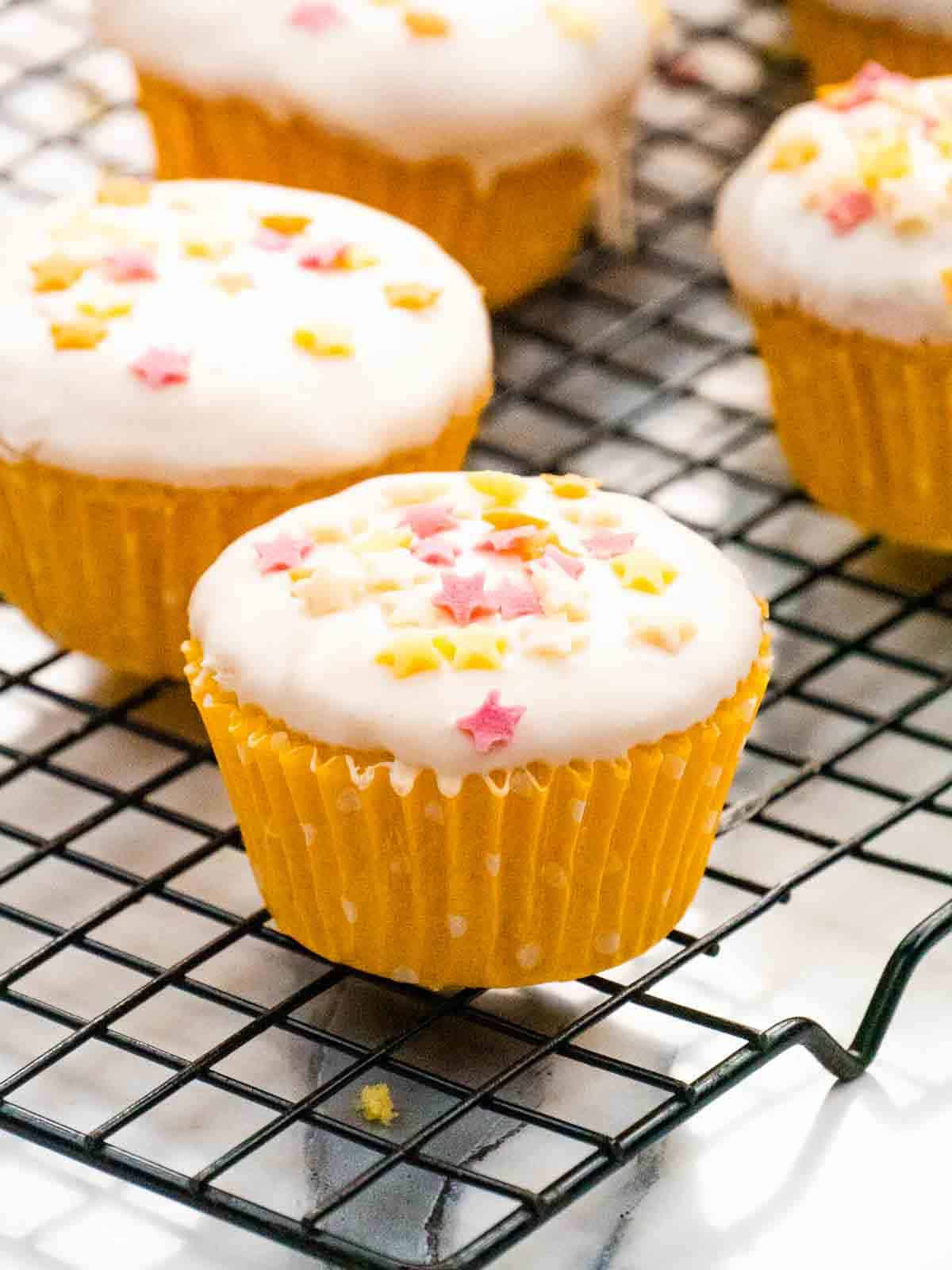 close up of an iced lemon drizzle cupcake in front of a row of cupcakes on wire rack