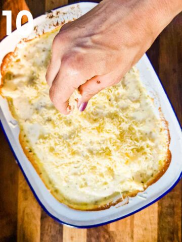 person sprinkling grated cheddar cheese om top of baked beef and potatoes before baking for a final 20 minutes