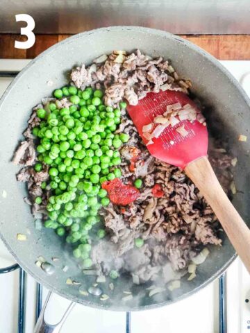 person mixing in garden peas, balsamic vinegar and tomato paste in a beef mixture in pan