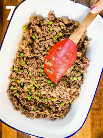 person spreading cooked beef mince on top of sliced potatoes