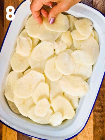 person placing a 2nd layer of potato slices on top of cooked beef layer in baking dish