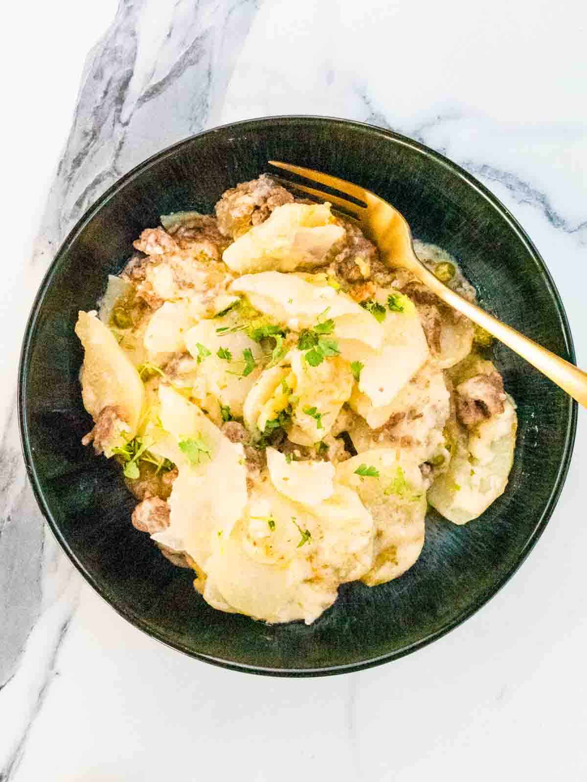 large black bowlful of beef potato bake with gold fork and garnished with fresh parsley