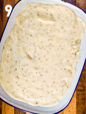 cheesy sauce topped on a potato and mince bake in large enamel baking dish before covering with boil and baking