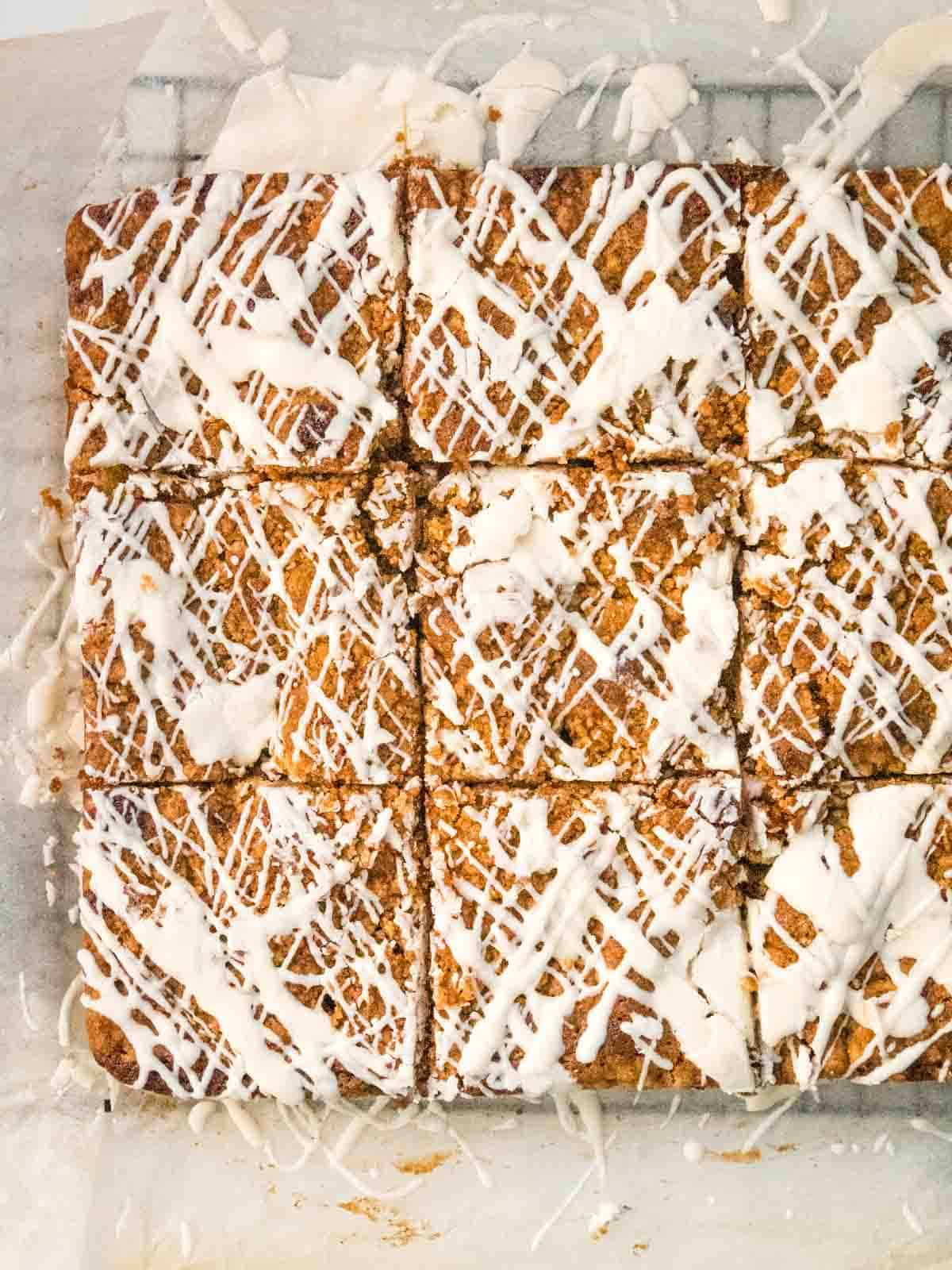 vanilla icing drizzled over rhubarb crumb cake and sliced for serving on white baking paper
