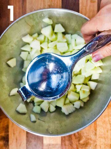person squeezing lemon juice over chopped apples in a medium bowl