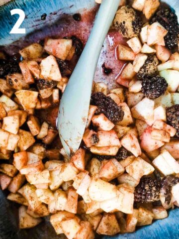 person mixing apples, blackberries, cinnamon and sugars while in a baking dish