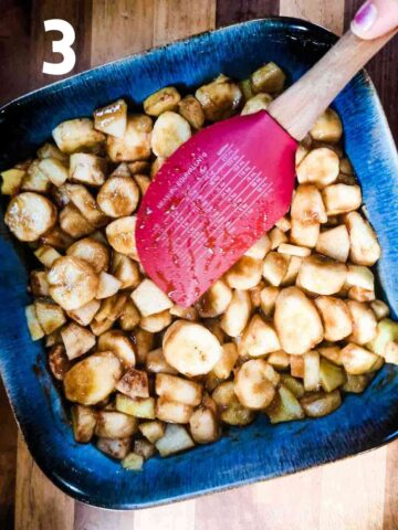 person levelling apple and banana mixed in sugar and cinnamon in a large square baking dish