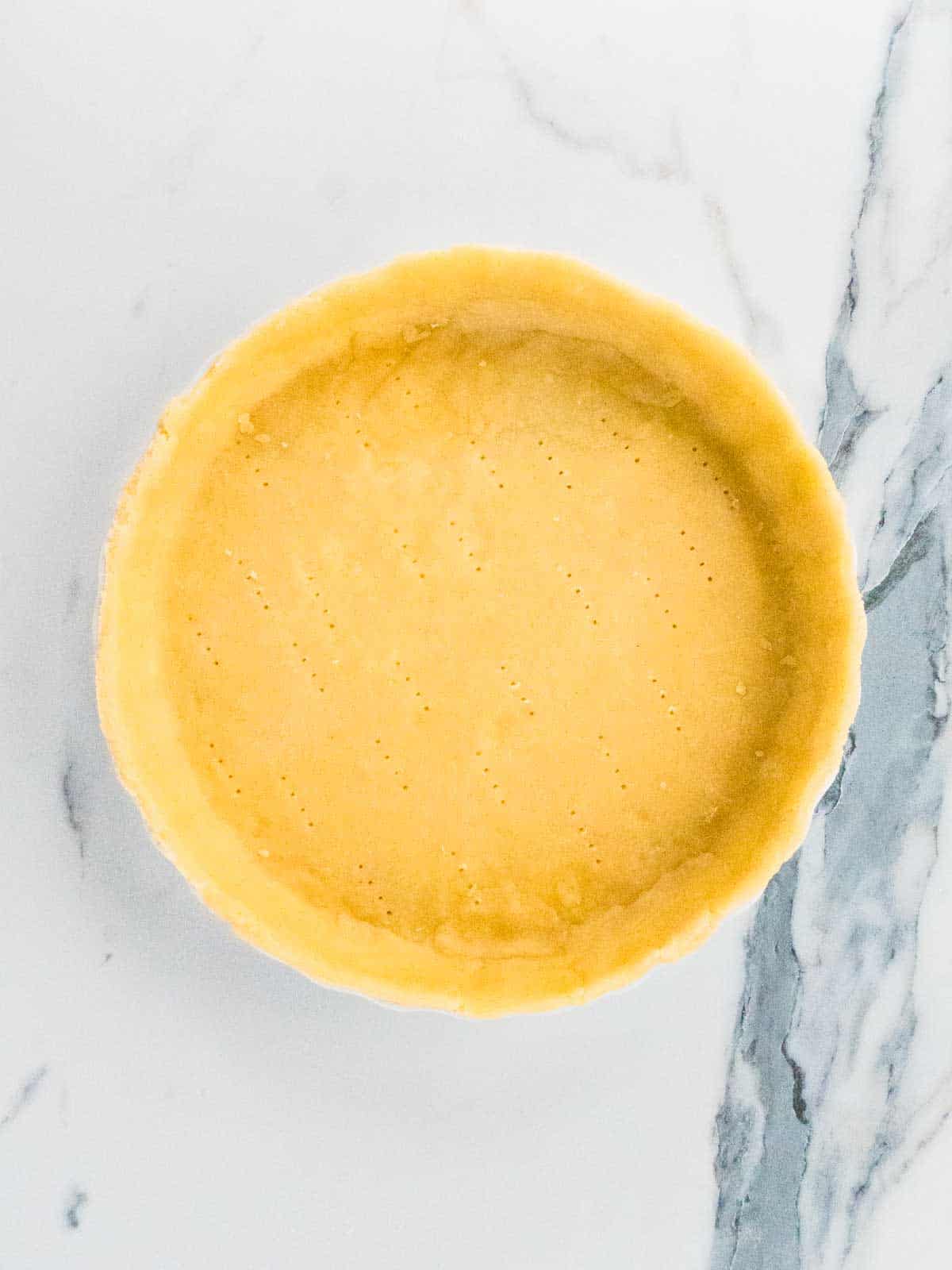 quiche dish lined with uncooked cheesy shortcrust pastry that has been pricked with a fork for blind baking