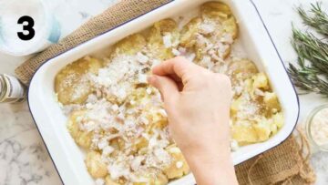 person sprinkling fresh rosemary leaves on crushed baby potatoes with parmesan, seasoning, and shallots