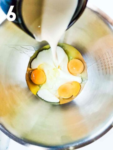 person pouring double cream into a large stainless steel mixing bowl with eggs