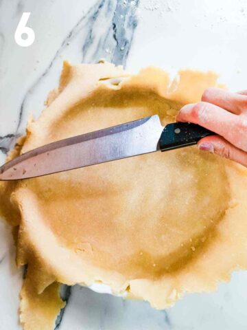 person trimming excess pastry from the top of a quiche pan