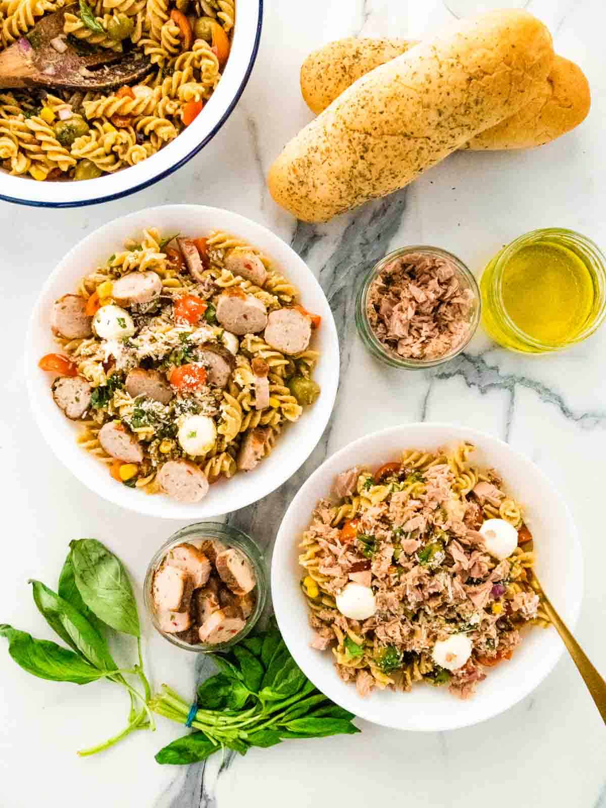 2 bowls of pasta freddo, each served with different meats like sliced cooked sausage and tuna flakes and crusty herby bread