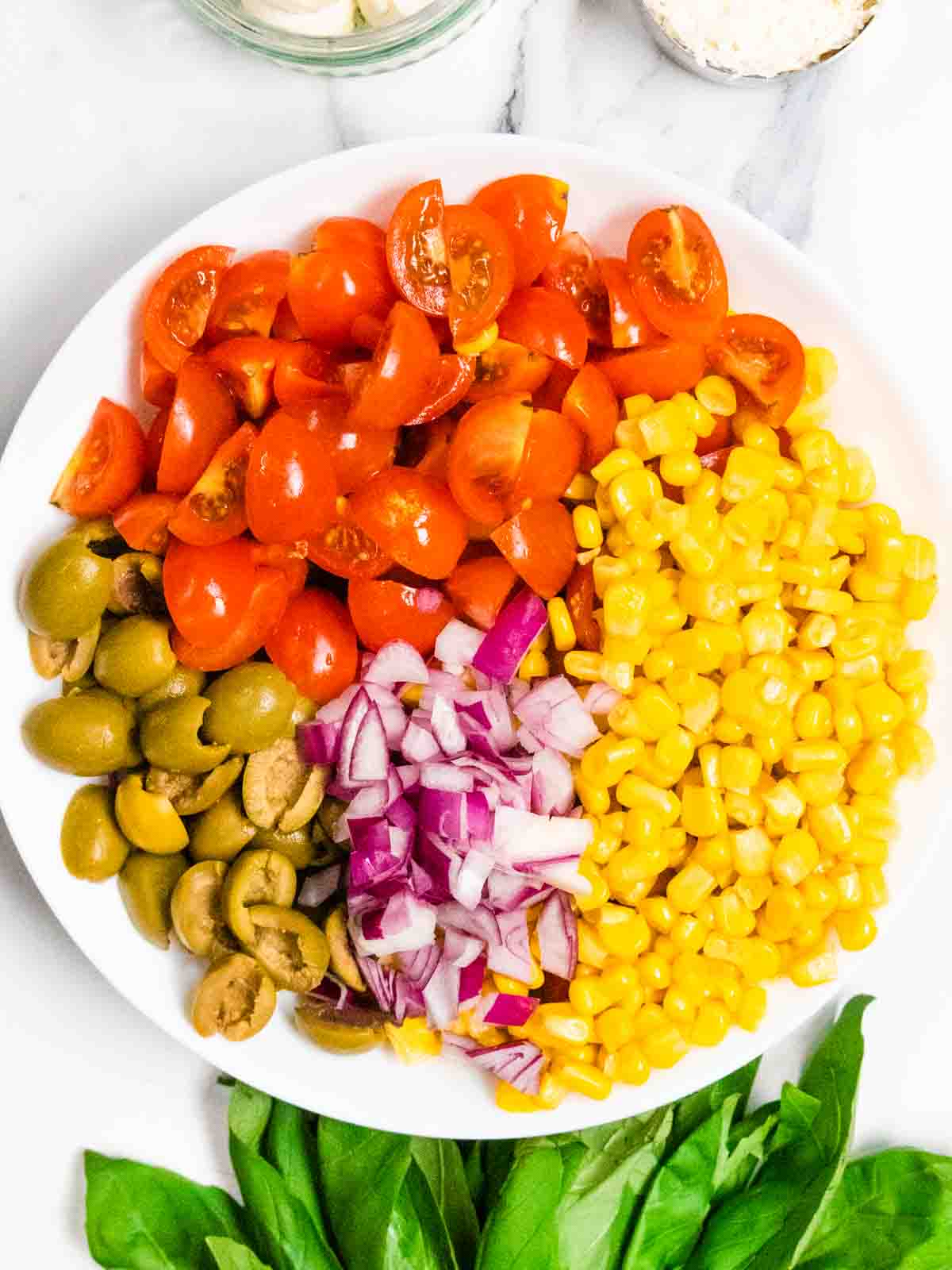 large white bowl full of chopped salad ingredients to stir into cold wholewheat fusilli pasta