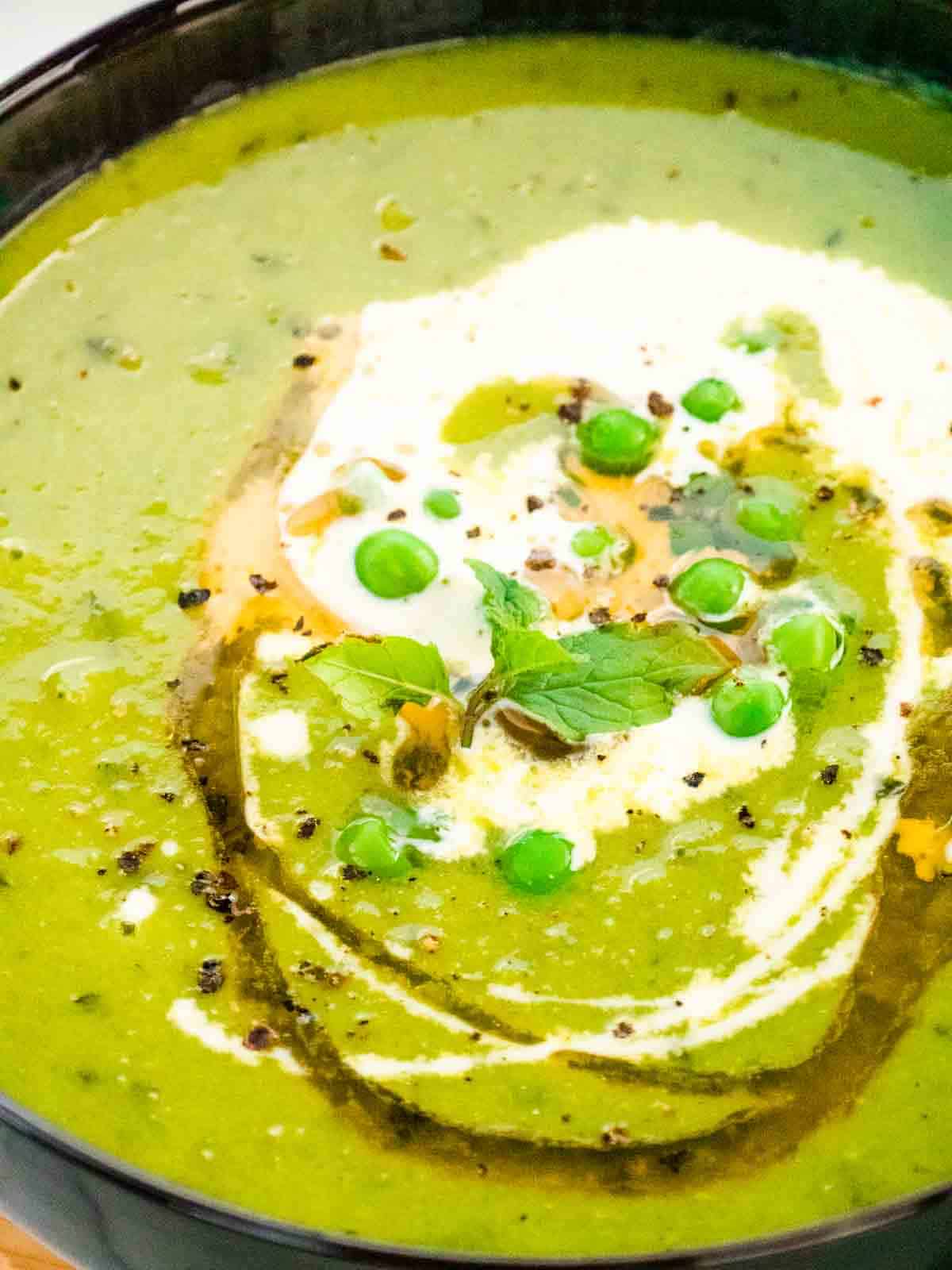 close up of pea mint soup with peas, oil and cream garnish