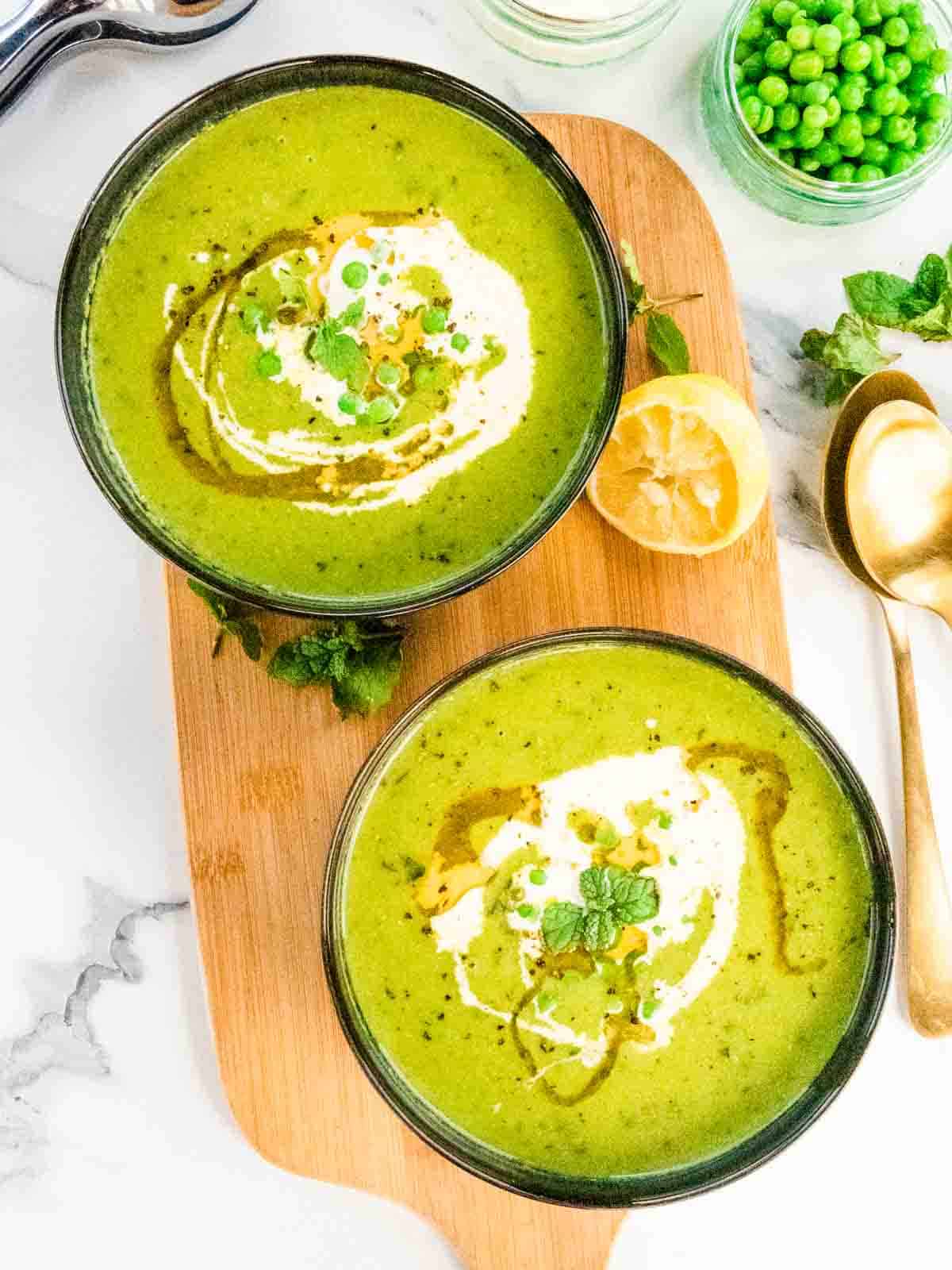 2 black bowls on wooden platter full of homemade pea mint soup
