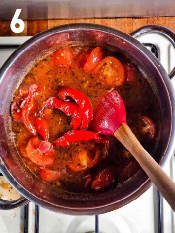 person stirring roasted peppers and tomatoes in a soup stock