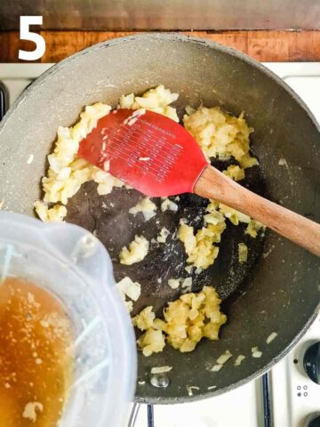 person making a roux with butter, onions and flour in a large frying pan while stirring in beef stock
