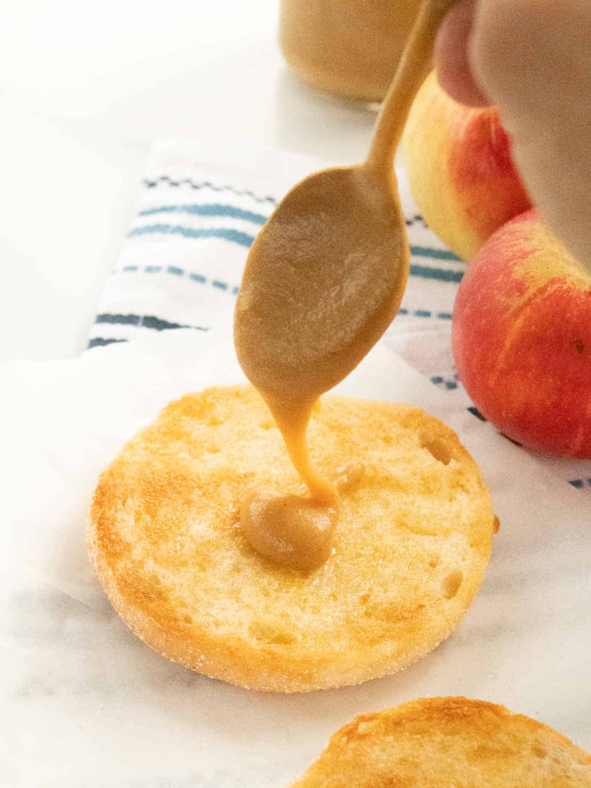 person drizzling homemade apple sauce on a toasted and buttered English muffin slice