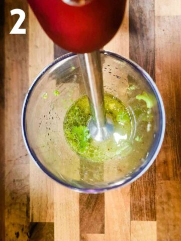person using an immersion blender blending avocados and herbs in a jug for salad dressing
