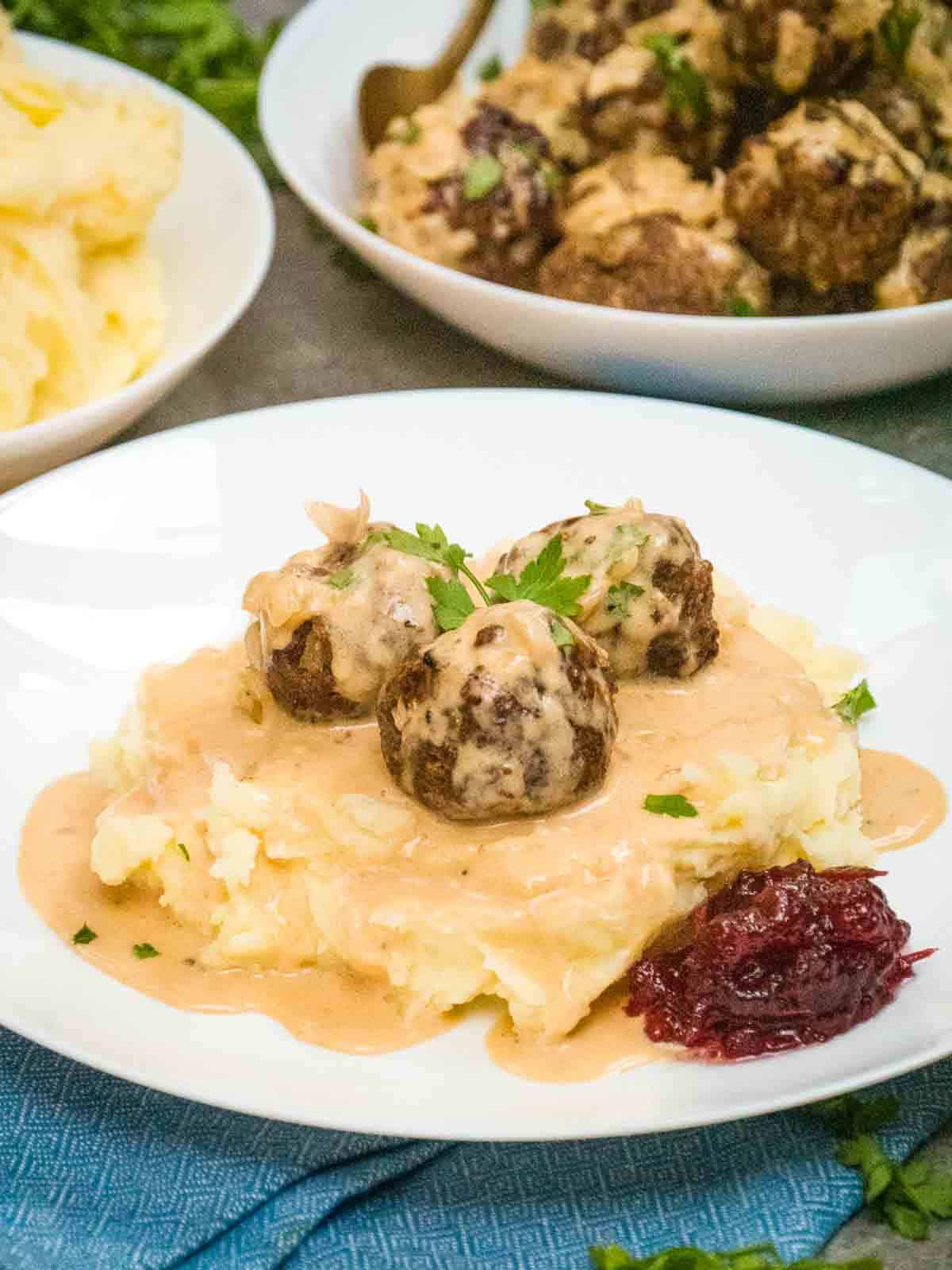 close up of 3 Finnish meatballs on creamy mashed potatoes with a creamy beef sauce on top and cranberrry sauce