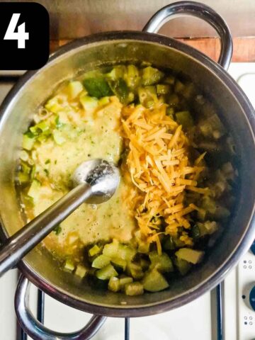 person using an immersion blender to blend courgette soup with grated soup until smooth